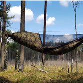 Bushmen Bushbed PRO Hammock in camo design suspended between trees with integrated mosquito net.